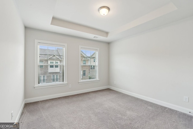 carpeted empty room featuring baseboards and a raised ceiling