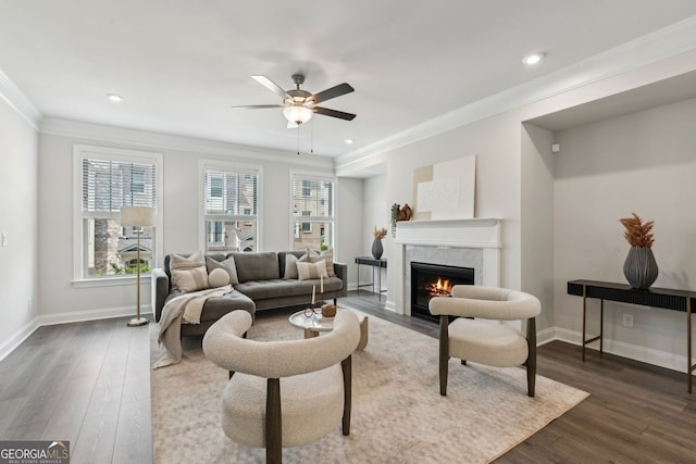 living area featuring crown molding, dark wood-style flooring, baseboards, ceiling fan, and a premium fireplace
