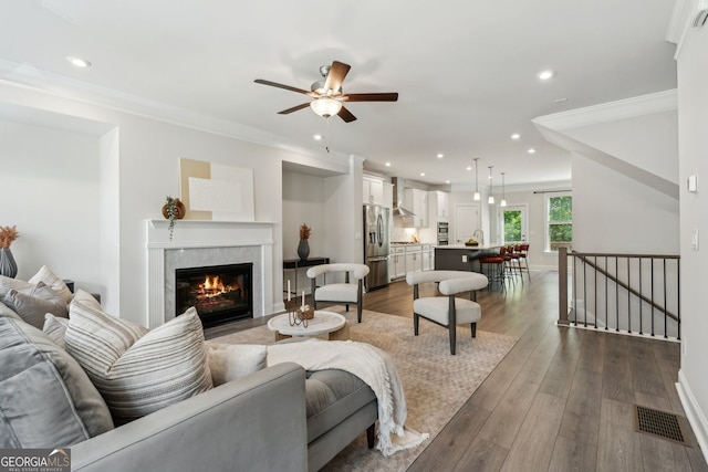 living area featuring crown molding, a premium fireplace, visible vents, and dark wood finished floors
