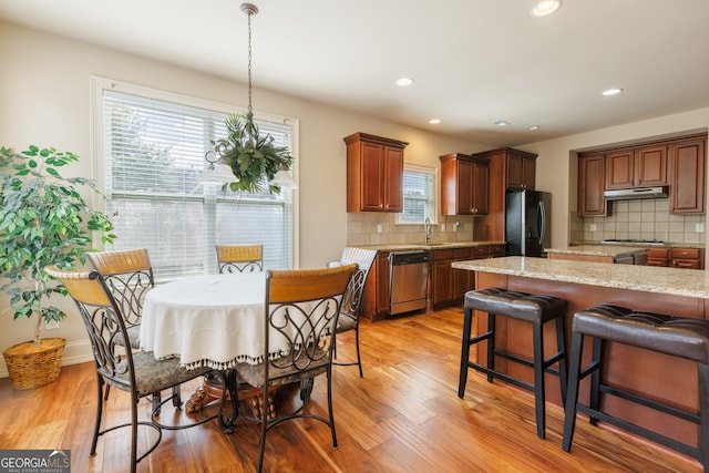 kitchen with appliances with stainless steel finishes, decorative backsplash, under cabinet range hood, and light wood-type flooring