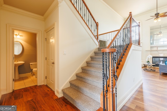 stairway featuring crown molding, a ceiling fan, baseboards, and wood finished floors