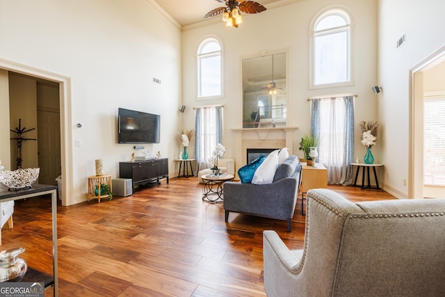 living room featuring crown molding, ceiling fan, visible vents, and a towering ceiling