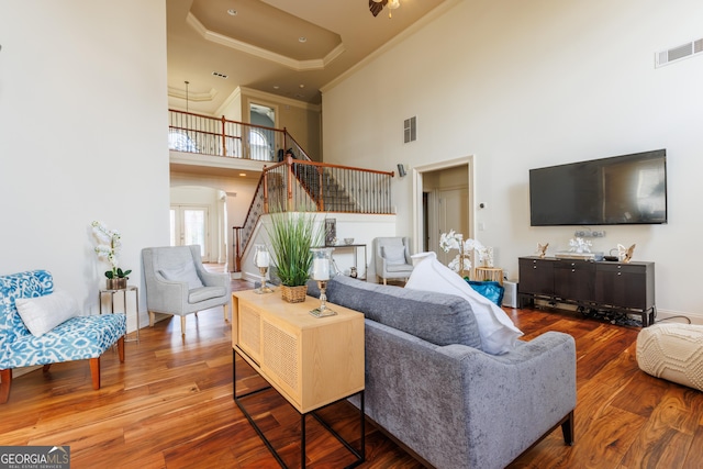 living room with a high ceiling, visible vents, ornamental molding, and wood finished floors