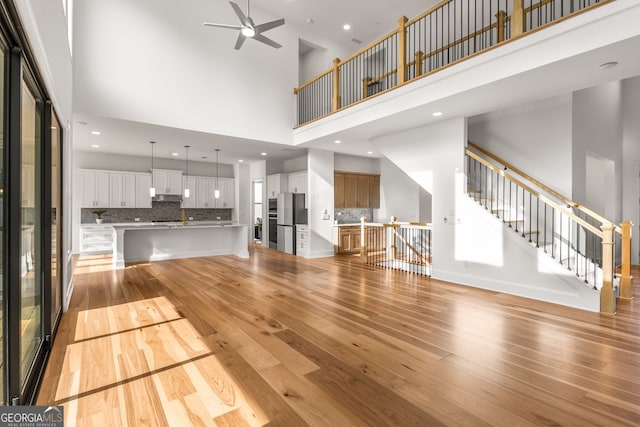 4039 Tallow Pl, Woodstock, GA 30188 - unfurnished living room featuring a towering ceiling, light wood-style flooring, ceiling fan, recessed lighting, and stairs