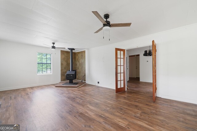 unfurnished living room featuring a wood stove, ceiling fan, and wood finished floors