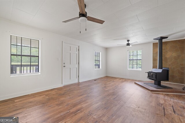 unfurnished living room featuring baseboards, a ceiling fan, wood finished floors, and a wood stove