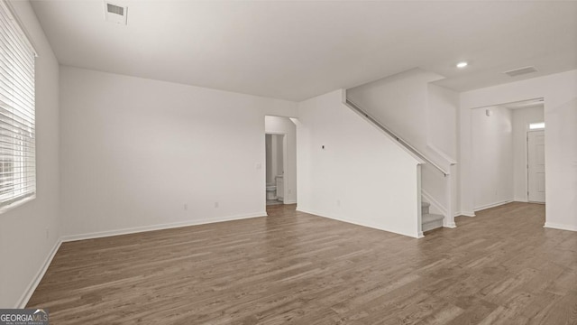 unfurnished living room with baseboards, stairs, wood finished floors, and visible vents