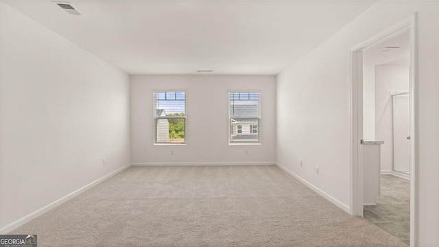 empty room with baseboards, visible vents, and light colored carpet