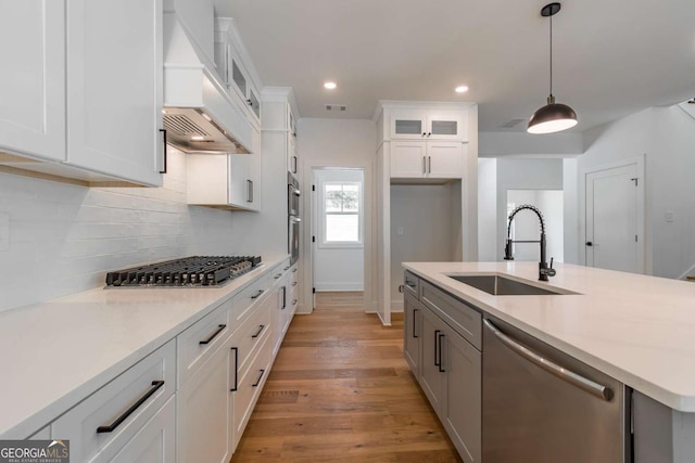 kitchen featuring a notable chandelier, appliances with stainless steel finishes, a sink, light wood-style floors, and decorative backsplash