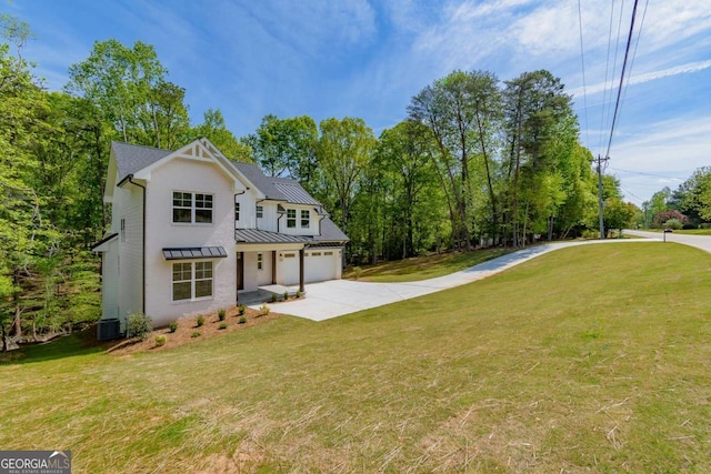 rear view of property featuring a standing seam roof, driveway, metal roof, a yard, and an attached garage