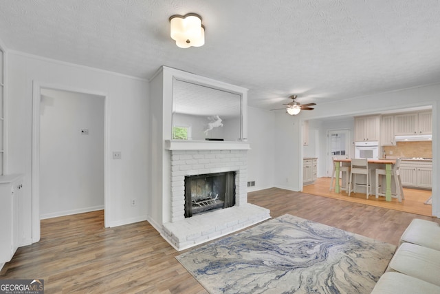 4420 Lake Breeze Dr, Stone Mountain, GA 30083 - living room featuring a brick fireplace, a textured ceiling, light wood-style flooring, a ceiling fan, and baseboards