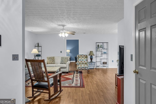 living room featuring a textured ceiling, ceiling fan, and wood finished floors