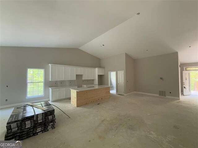 kitchen featuring baseboards, white cabinets, a kitchen island, and lofted ceiling