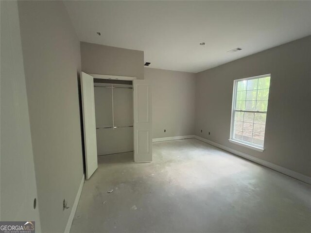 unfurnished bedroom with concrete flooring, baseboards, visible vents, and a closet