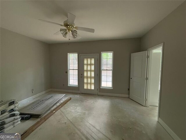 unfurnished room featuring ceiling fan, unfinished concrete flooring, and baseboards