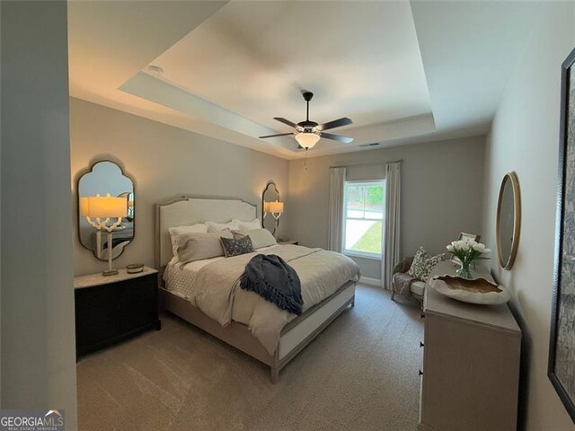 bedroom with light colored carpet, a raised ceiling, and ceiling fan
