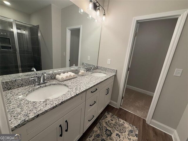 bathroom with double vanity, a stall shower, a sink, and wood finished floors