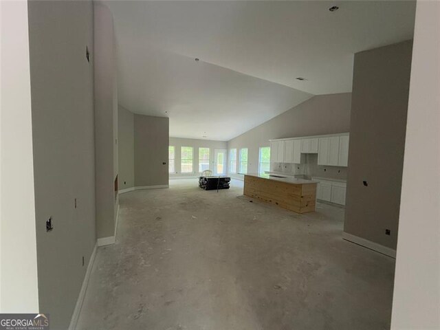 living area featuring baseboards, lofted ceiling, and unfinished concrete flooring