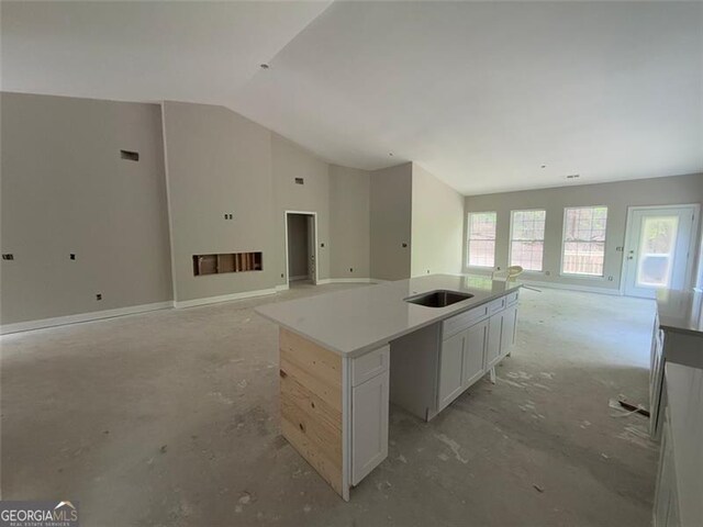 kitchen featuring a sink, open floor plan, lofted ceiling, white cabinetry, and an island with sink