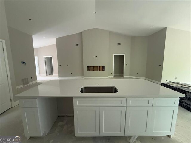 kitchen with a sink, light countertops, white cabinetry, open floor plan, and vaulted ceiling
