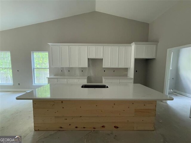 kitchen featuring a sink, high vaulted ceiling, baseboards, white cabinetry, and an island with sink
