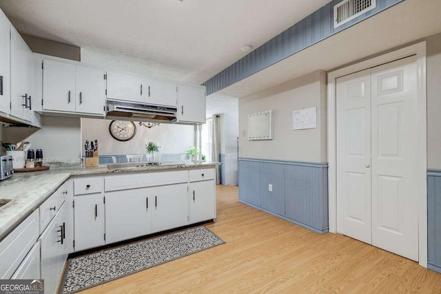 kitchen featuring white cabinets, under cabinet range hood, light wood finished floors, and black electric stovetop