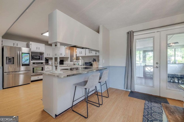kitchen featuring appliances with stainless steel finishes, a wainscoted wall, a peninsula, white cabinetry, and light wood-type flooring