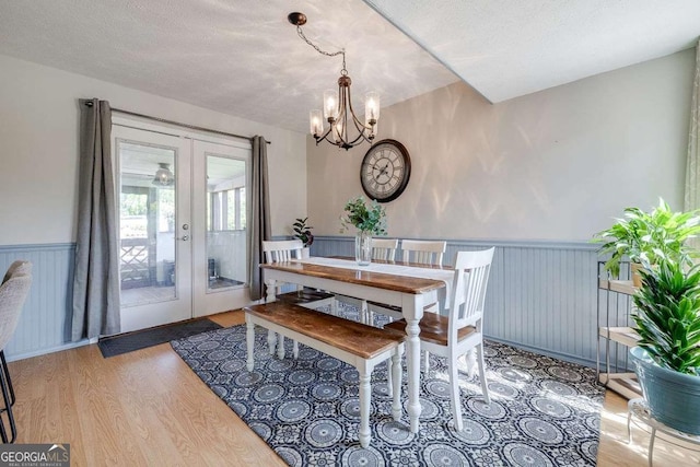 dining room featuring french doors, a textured ceiling, wood finished floors, a wainscoted wall, and a notable chandelier