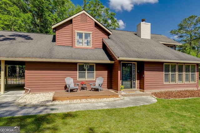 rear view of house with a chimney, roof with shingles, a deck, a carport, and a yard