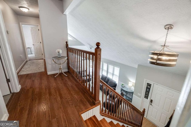 hall with a notable chandelier, a textured ceiling, baseboards, an upstairs landing, and wood finished floors