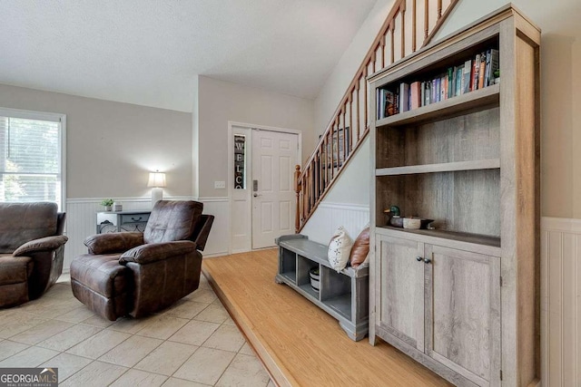 living room with wainscoting, a decorative wall, stairs, and light tile patterned flooring
