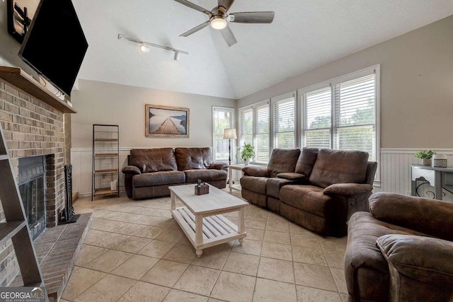living room featuring track lighting, wainscoting, a brick fireplace, ceiling fan, and vaulted ceiling