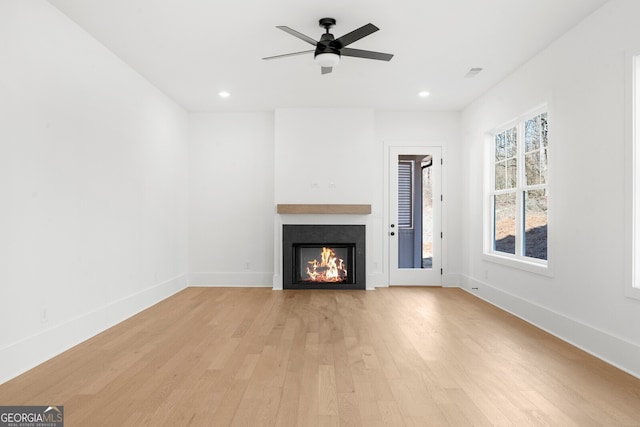 unfurnished living room with visible vents, light wood-style flooring, a ceiling fan, baseboards, and a lit fireplace