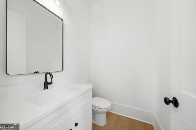 half bathroom with vanity, baseboards, wood finished floors, and toilet