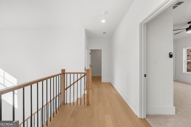 hall featuring visible vents, light wood-style floors, baseboards, recessed lighting, and an upstairs landing