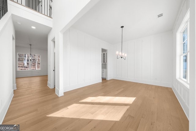 unfurnished dining area with visible vents, baseboards, light wood finished floors, a notable chandelier, and a decorative wall
