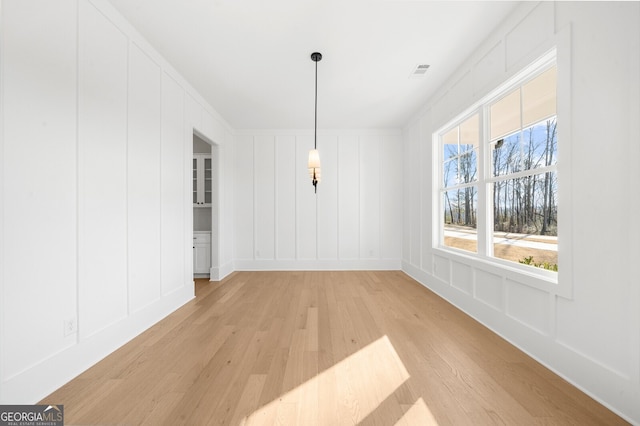 unfurnished dining area featuring light wood-style floors, a decorative wall, and visible vents