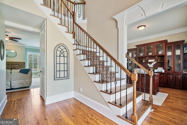 stairway featuring crown molding, hardwood / wood-style floors, baseboards, ceiling fan, and a high ceiling