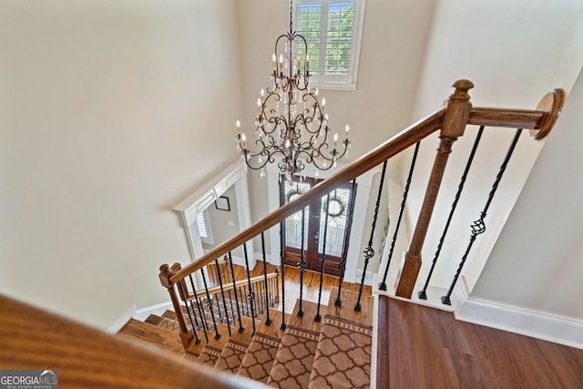 stairway featuring baseboards, an inviting chandelier, and wood finished floors