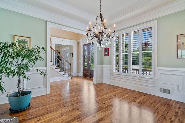 unfurnished dining area featuring an inviting chandelier, crown molding, stairs, wood finished floors, and a wainscoted wall
