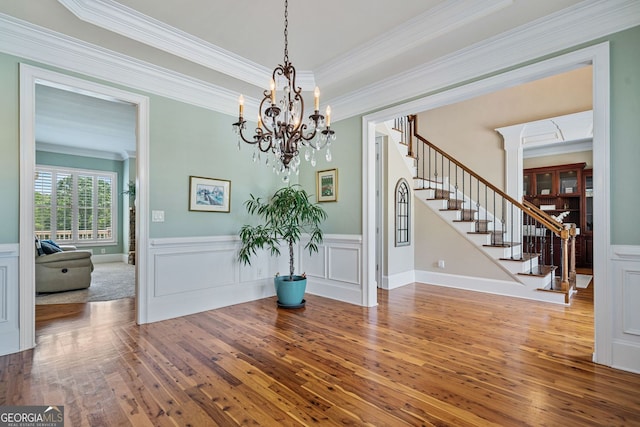 unfurnished dining area with crown molding, wainscoting, wood-type flooring, an inviting chandelier, and stairs