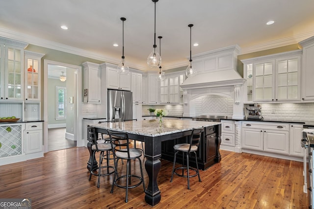 kitchen featuring a kitchen island, hanging light fixtures, wood-type flooring, stainless steel fridge, and a breakfast bar