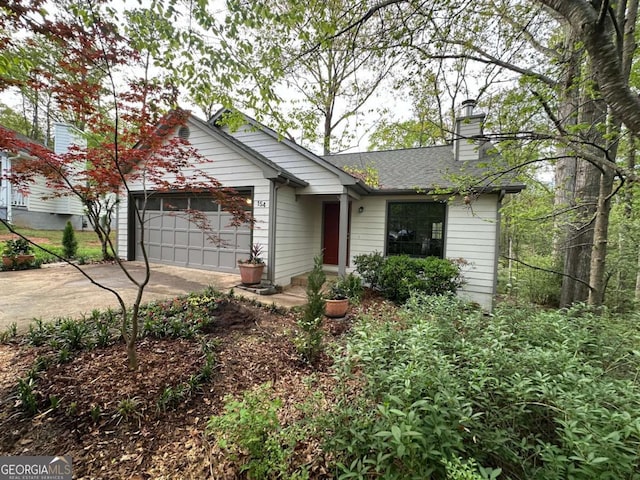 view of front of house featuring an attached garage, a shingled roof, a chimney, and concrete driveway