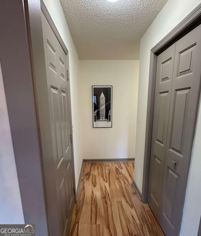 hallway with a textured ceiling, visible vents, and light wood finished floors