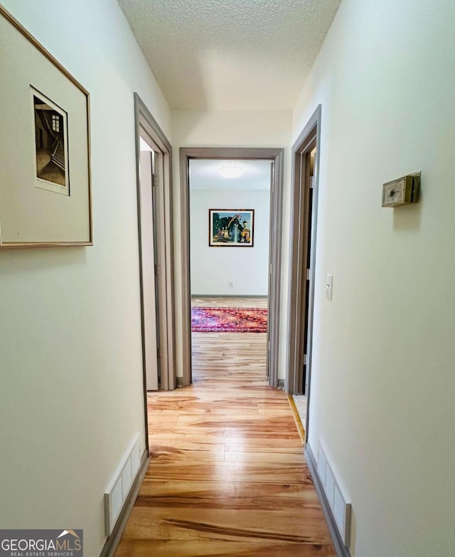 spare room featuring baseboards, a textured ceiling, visible vents, and wood finished floors