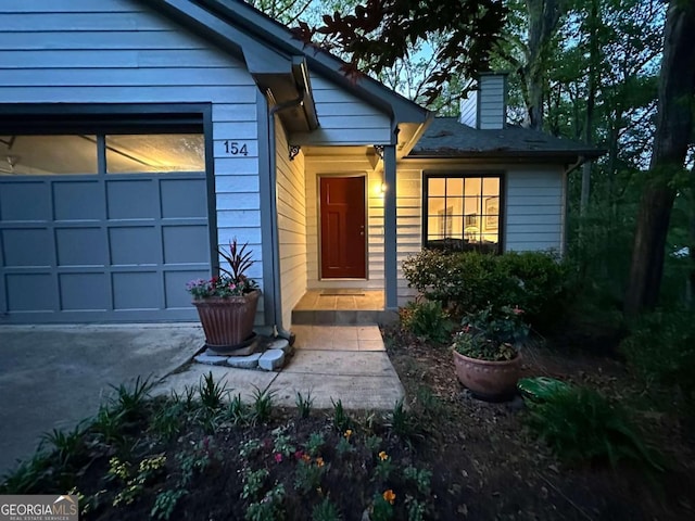 doorway to property featuring a chimney, an attached garage, and driveway