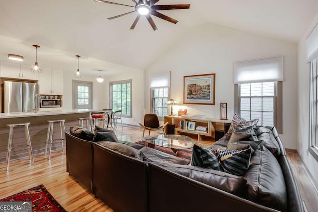 living room featuring vaulted ceiling, a ceiling fan, and light wood-style flooring