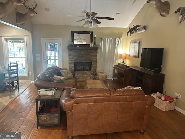 living area featuring a ceiling fan, vaulted ceiling, wood finished floors, and a fireplace