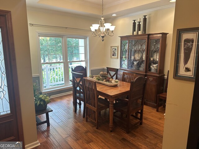 dining area featuring crown molding, a notable chandelier, a raised ceiling, and dark wood-type flooring