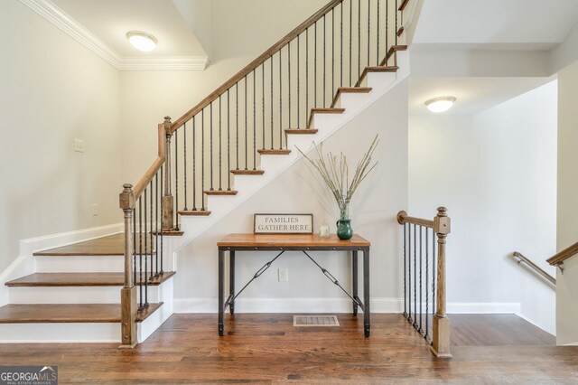 staircase with baseboards, ornamental molding, wood finished floors, and visible vents